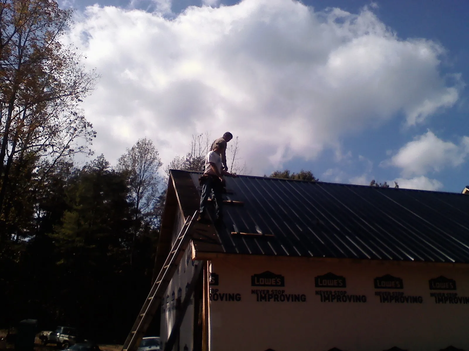 Roofer fastening dark metal panels high against a cloudy sky, from a Roof Inspection job in Ardmore