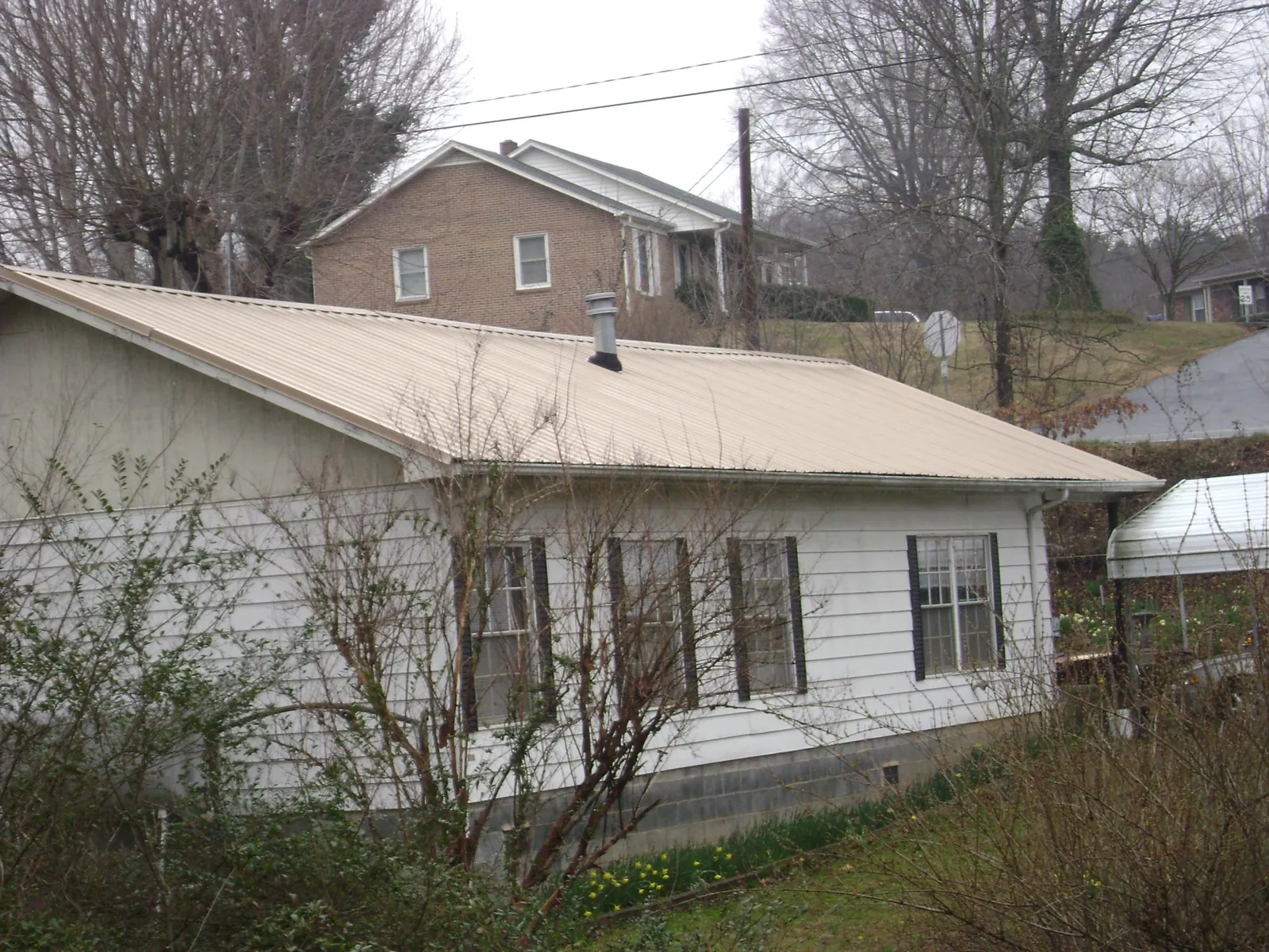 Tan metal roof on a white sided house set into a hillside — Commercial Roofing by Roofing Brothers in Ardmore