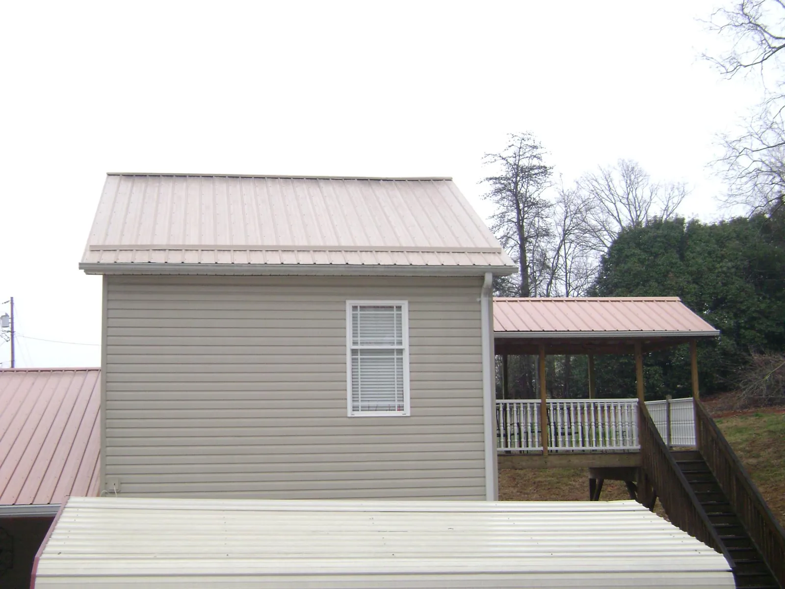 Tan metal roofs on a two story addition and attached porch, from a Roof Replacement job in Ardmore